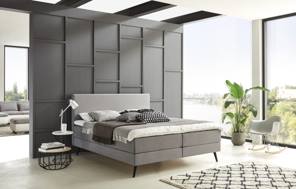 Ein modernes Schlafzimmer mit einem Bett, umgeben von schönen Deko-Elementen in einem lichtdurchfluteten Raum mit einer stilvollen, modernen Trennwand.